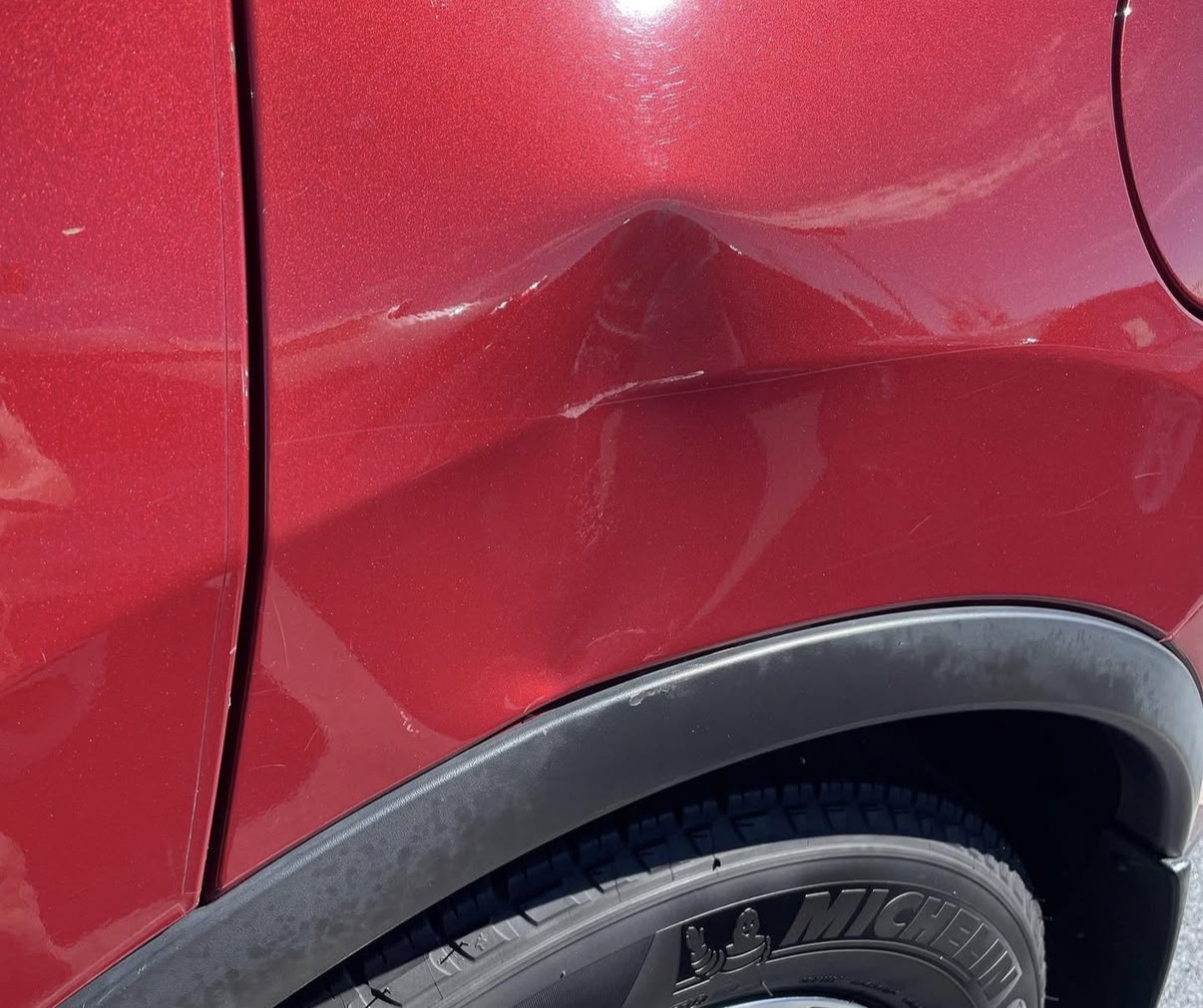Red SUV rear quarter panel with a dent near the fuel door before paintless dent repair