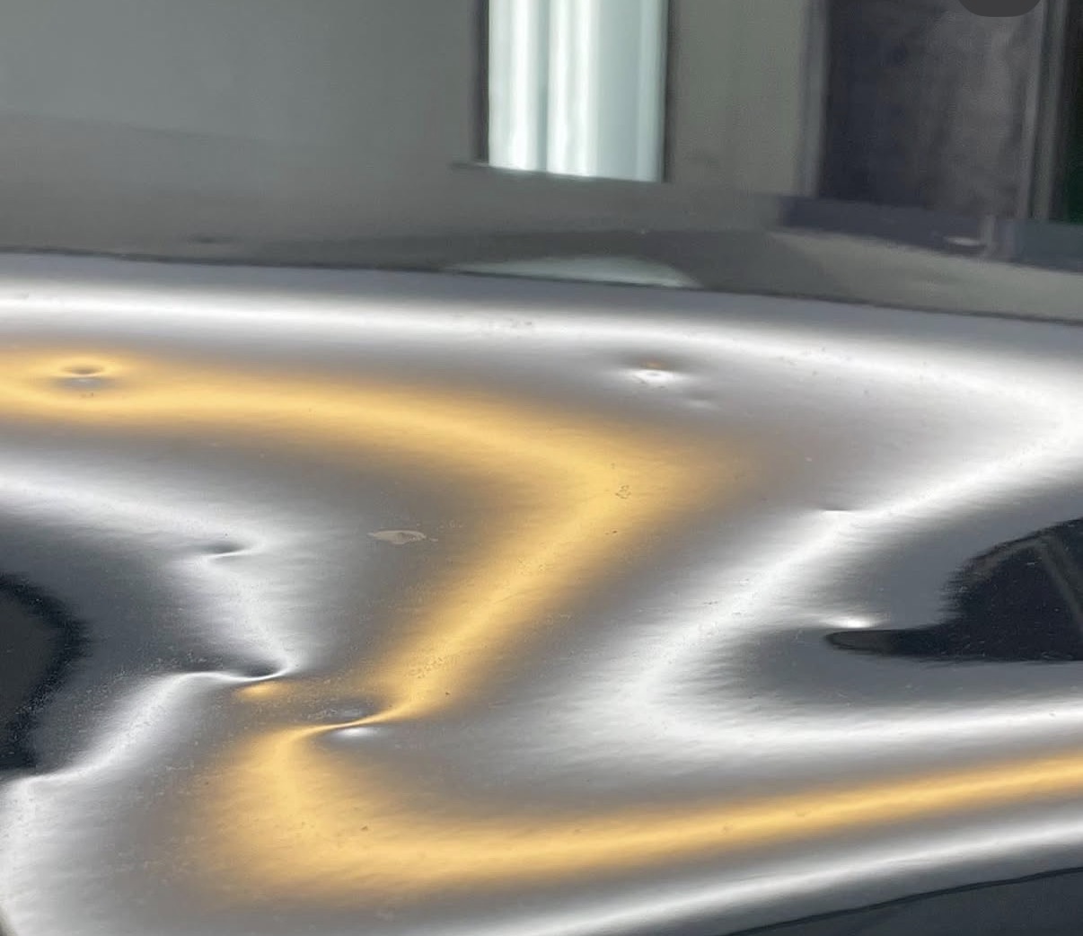 Vehicle panel with multiple dents shown on a reflection board before paintless dent repair